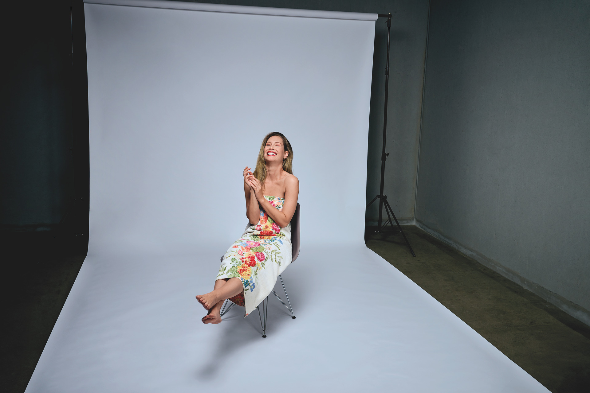 Frau in Blumenmuster-Kleid lächelnd im Studio – Luxuriöses FEILER Handtuch der Kollektion SUMMER DAY als Lifestyleaufnahme aus Original FEILER-Chenille, Made in Germany.