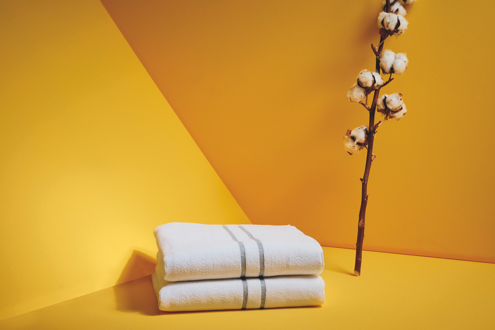 Weißes Handtuchset vor gelbem Hintergrund – Luxuriöses FEILER Handtuch der Kollektion LA GLAMOUR als Lifestyleaufnahme aus Original FEILER-Chenille, Made in Germany.