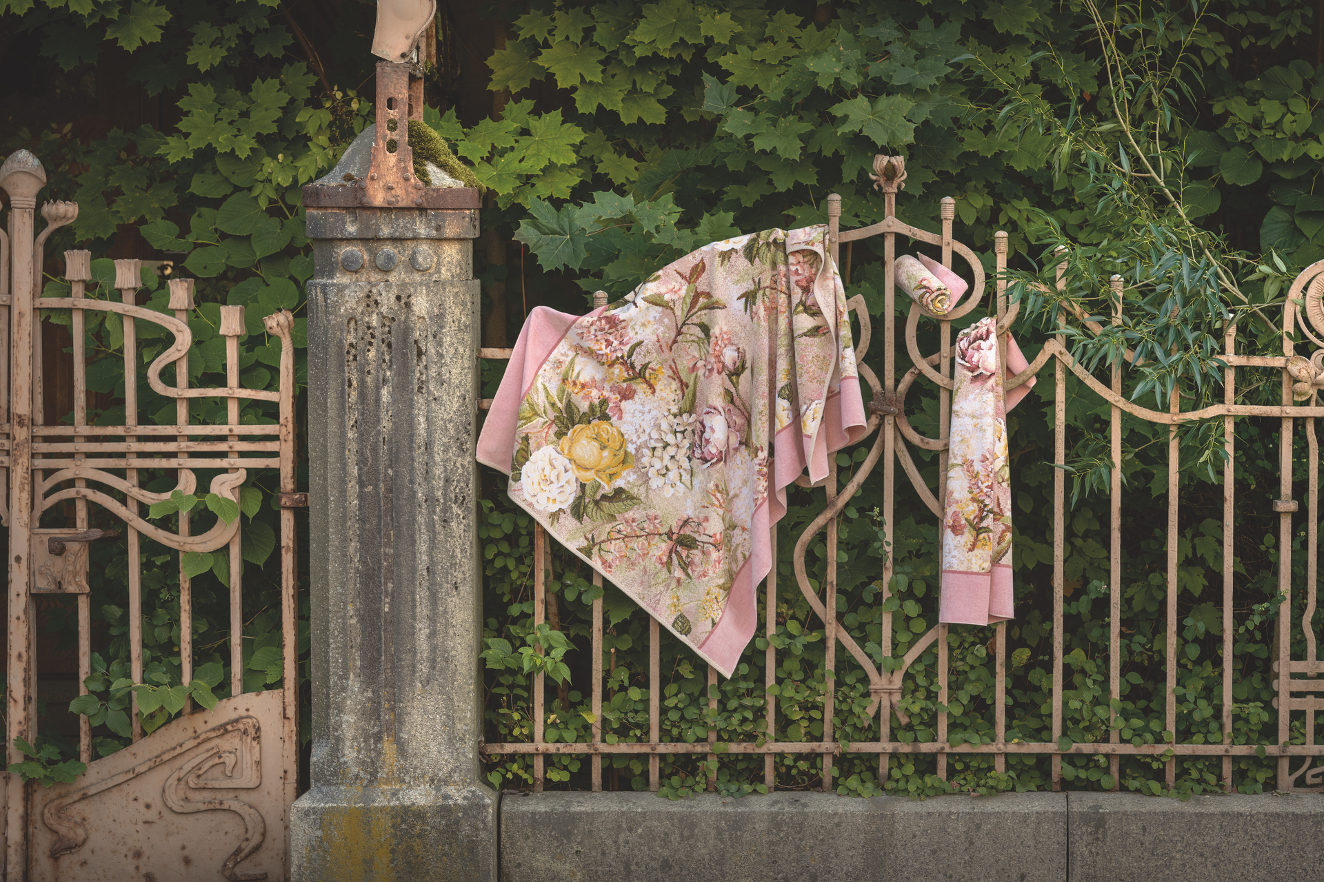 Floral-patterned textiles draped on an ornate metal fence, leafy background; no models present.