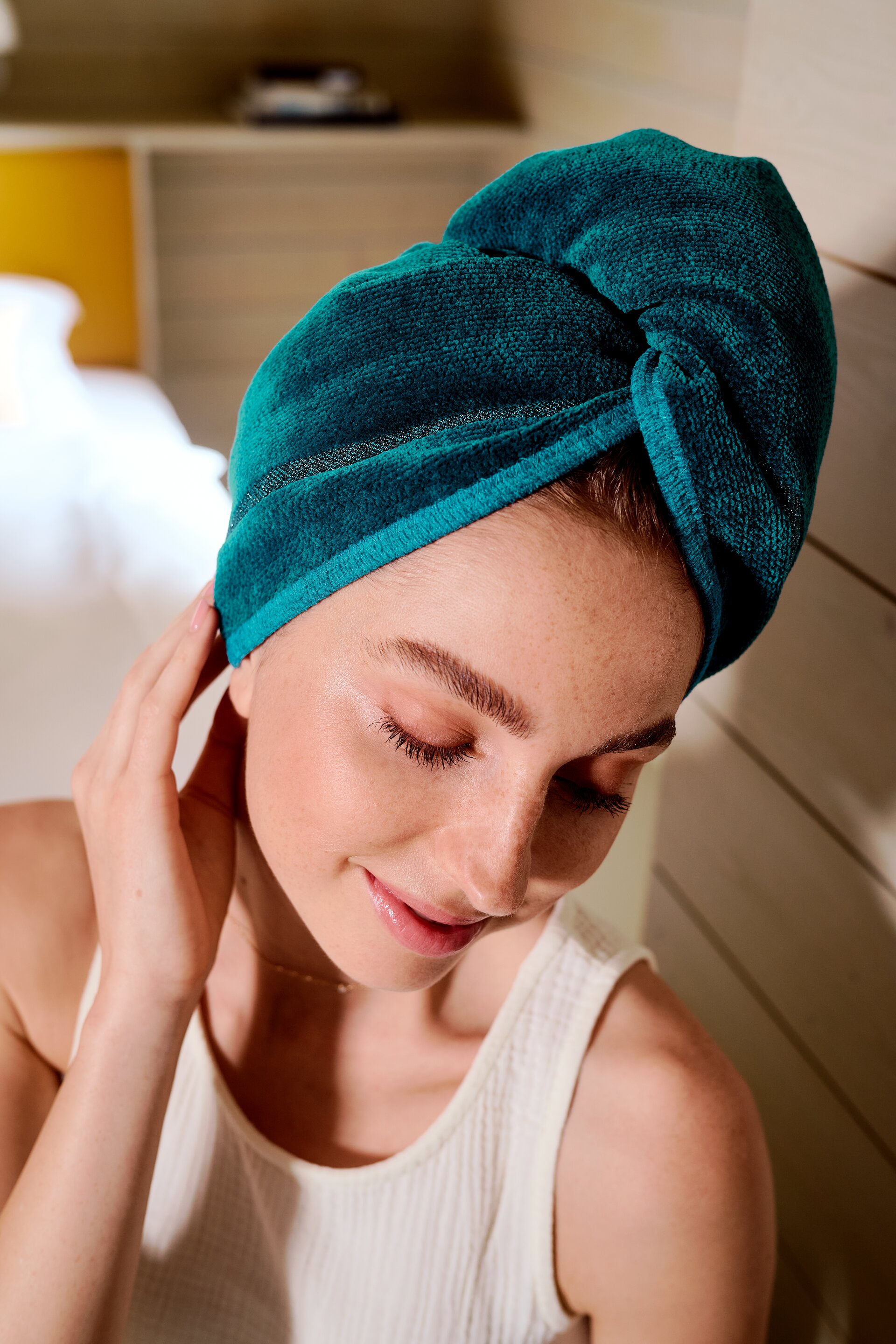 Adult woman with a teal fabric twist on her head, fine texture visible, wearing a white top, smiling softly.