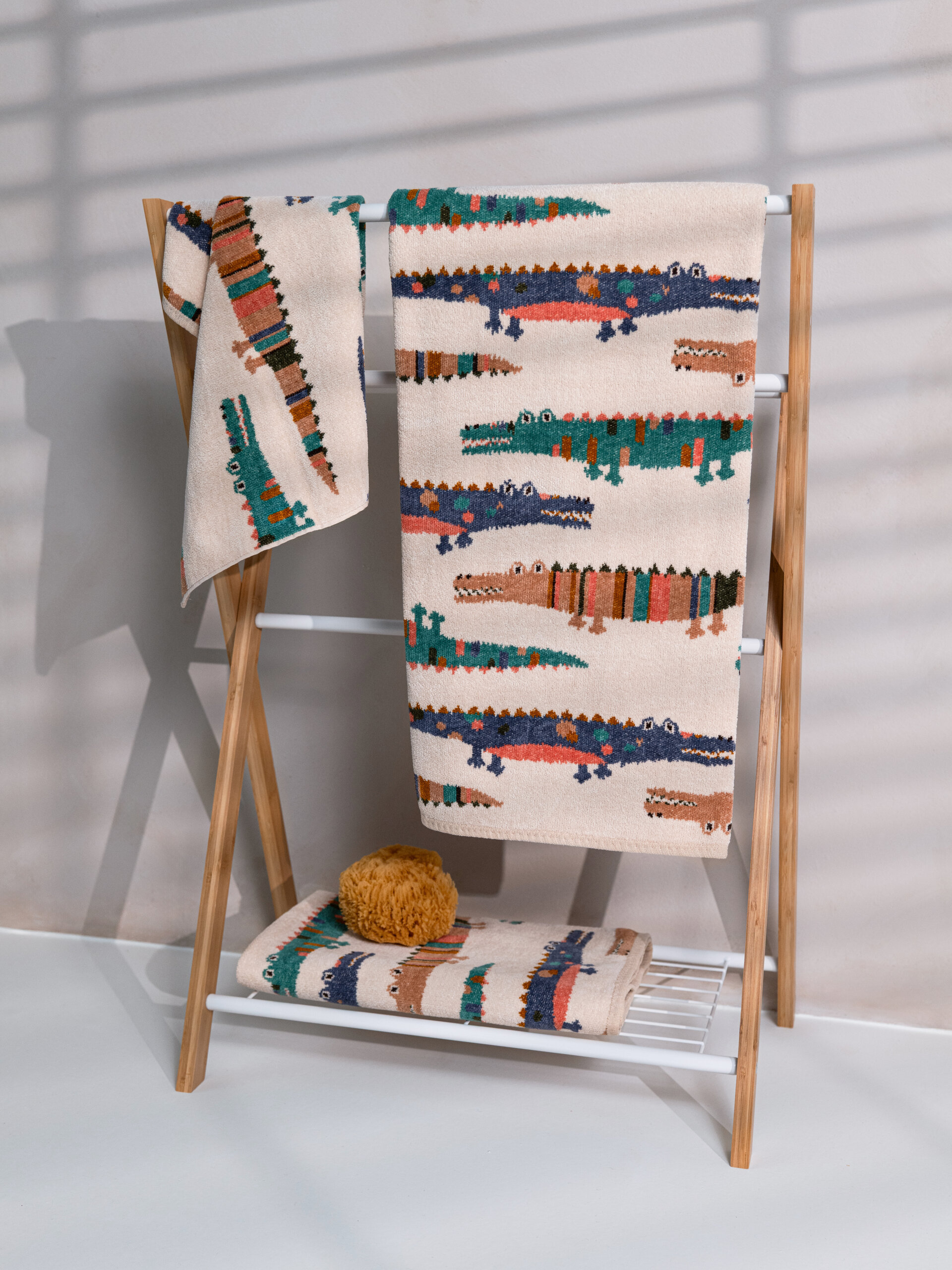Set-Ansicht verschiedener FEILER KROKO Babytextilien aus Original FEILER-Chenille, dekorativ mit einem Badeschwamm arrangiert.