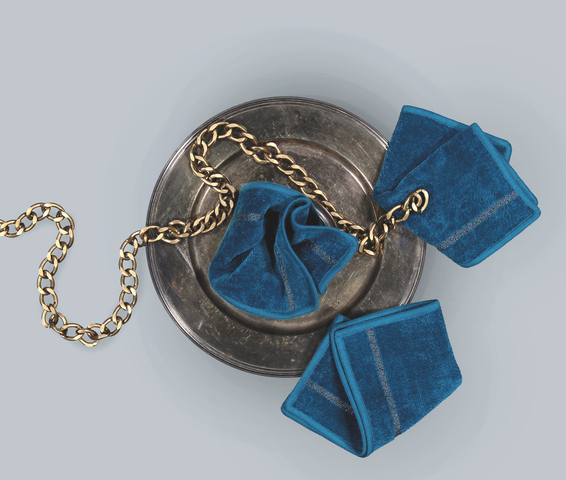Blue chenille fabric with a subtle grey stripe, elegantly draped over a silver platter with gold chain accent.