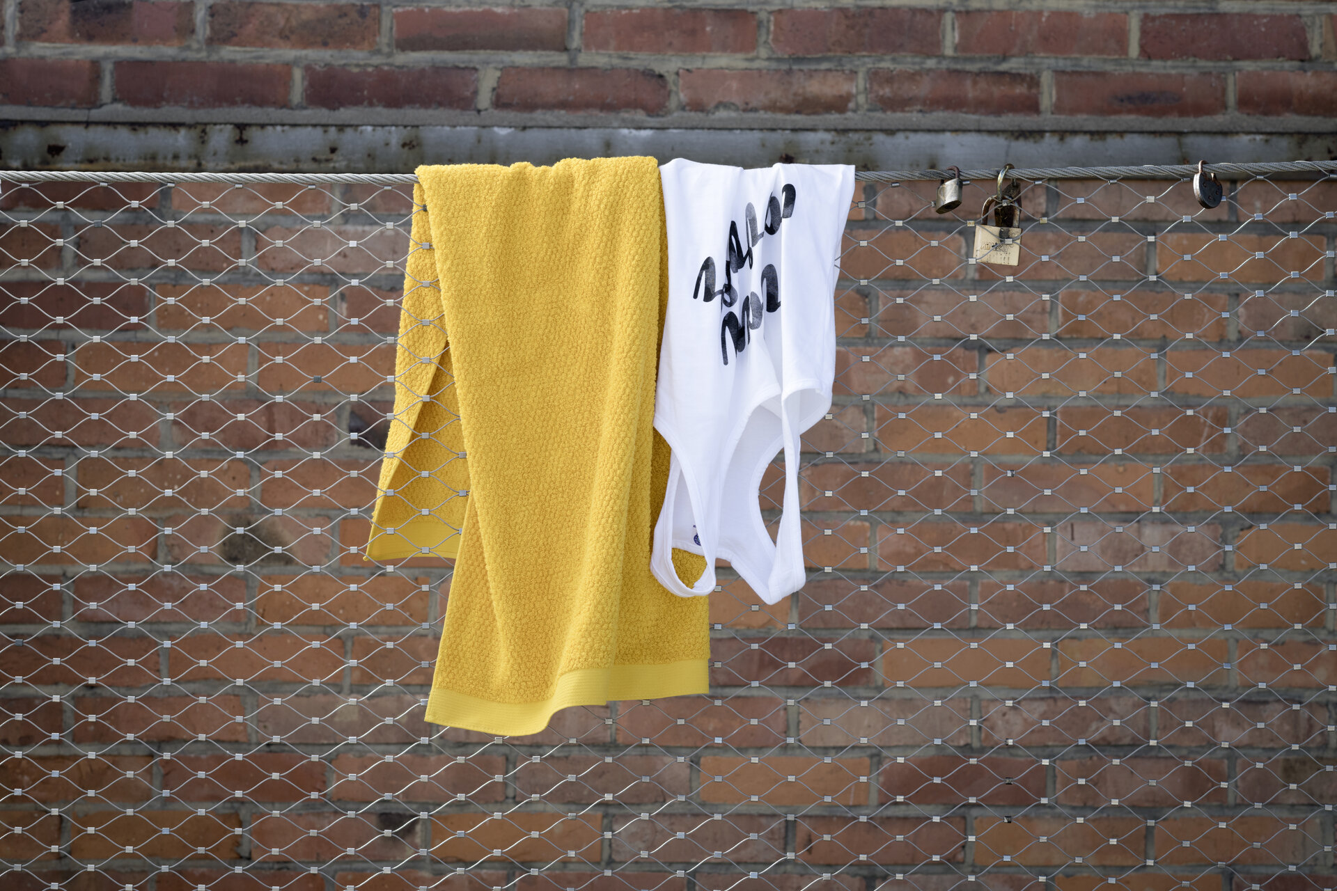 Gelbes Baumwolltuch an Metallzaun – Luxuriöses FEILER Handtuch der Kollektion IBIZA als Lifestyleaufnahme aus Original FEILER-Chenille, Made in Germany.