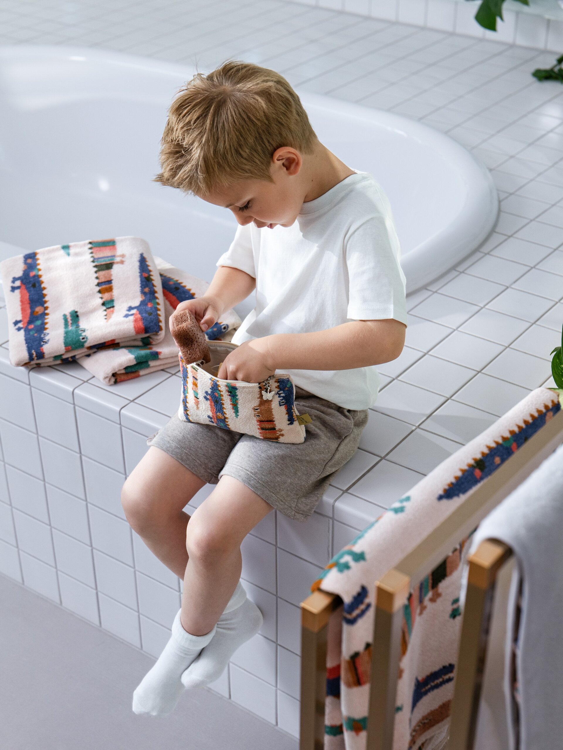 Lifestyle-Aufnahme mit FEILER KROKO Badetuch mit Kapuze, Pflegetuch und Täschchen M10, von einem Model an der Badewanne präsentiert.