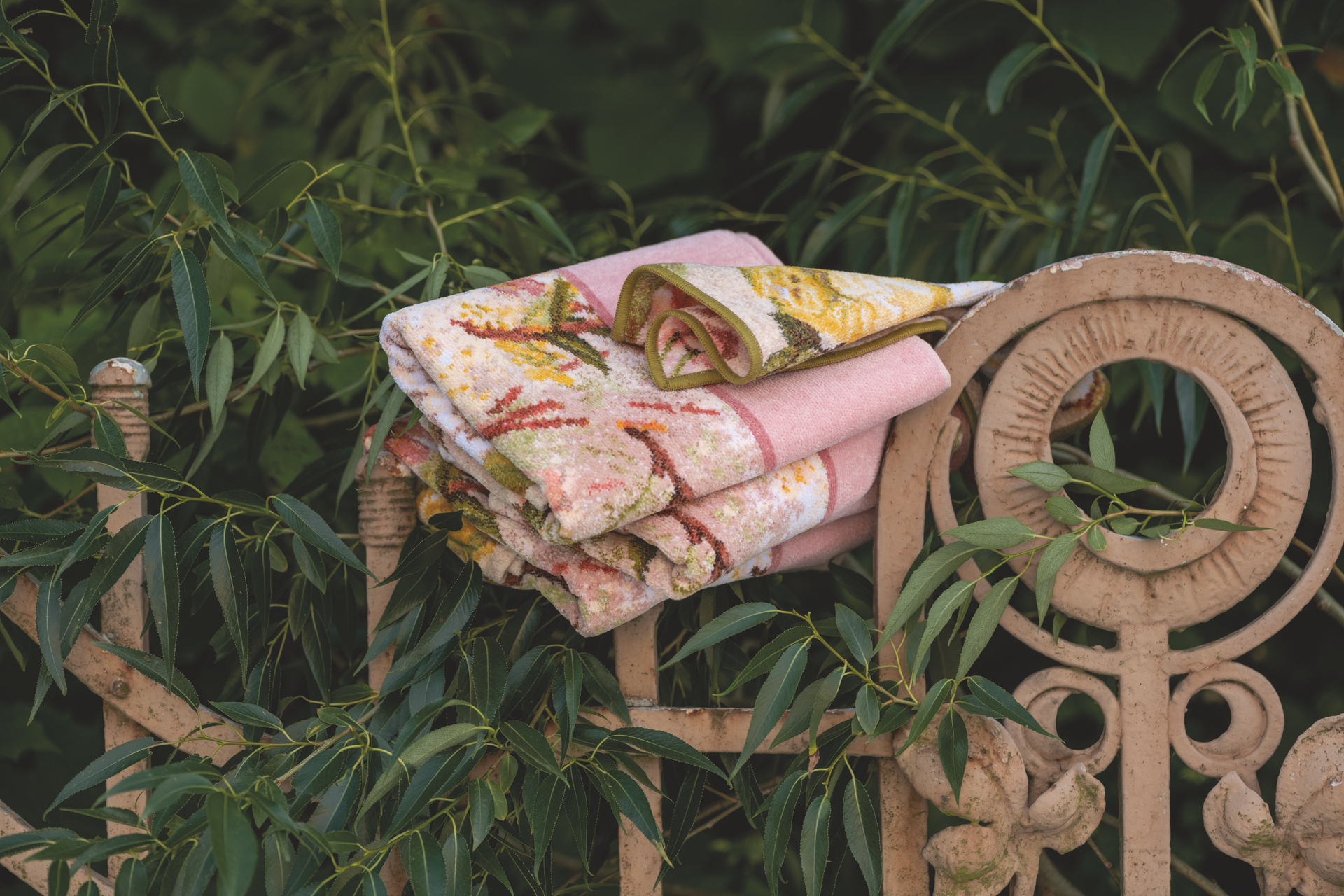 Floral-patterned chenille textiles in pink and green draped over a decorative wrought iron fence.