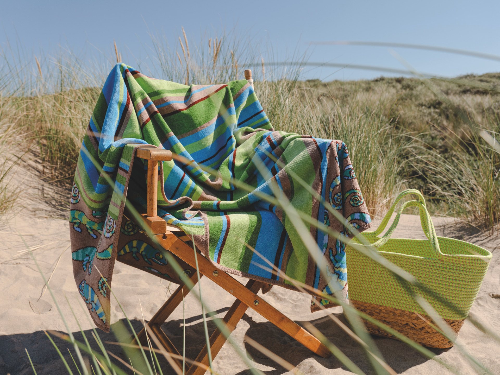 Strandtuch mit buntem Muster am Strand – Luxuriöses FEILER Strandtuch der Kollektion IGUANIA als Lifestyleaufnahme aus Original FEILER-Chenille, Made in Germany.