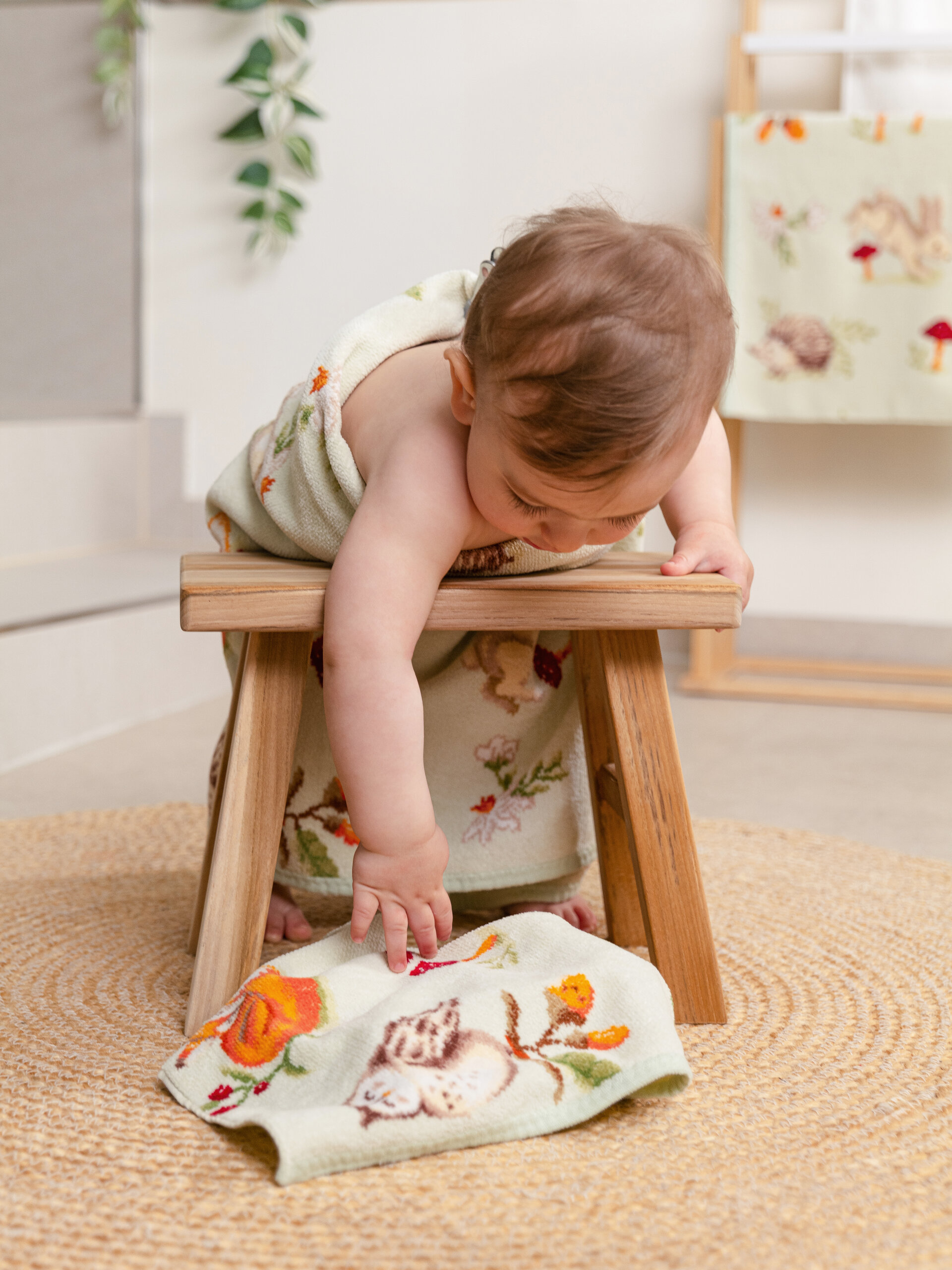 Baby mit gemustertem Handtuch auf Hocker – Luxuriöses FEILER Handtuch der Kollektion FOREST TALES als Lifestyleaufnahme aus Original FEILER-Chenille, Made in Germany.