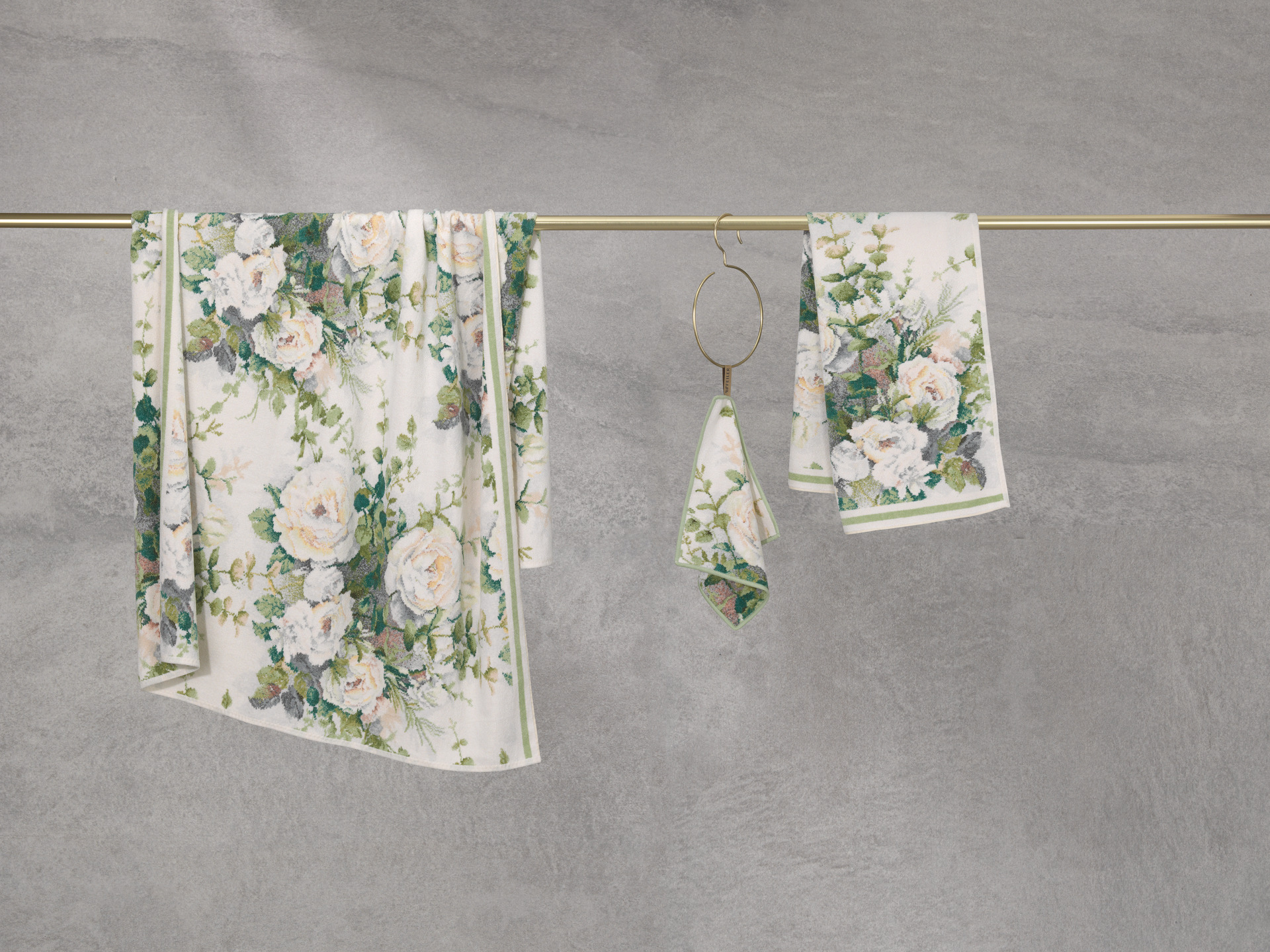 Floral print textiles with roses and green leaves hanging on a bar against a grey background.