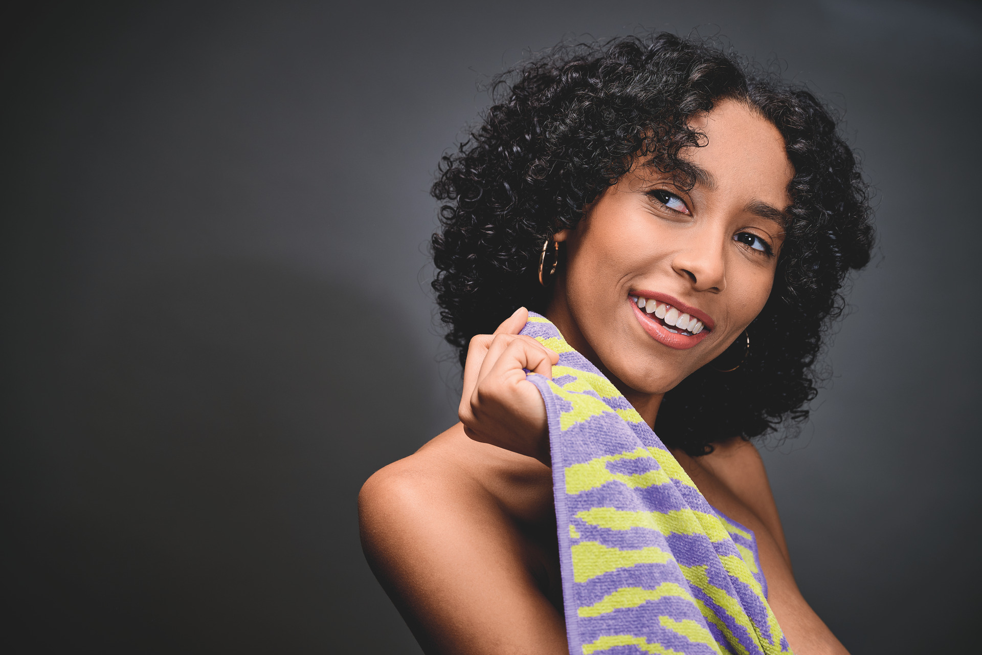 Young adult woman with curly hair holds textured towel in purple and green with wavy pattern.