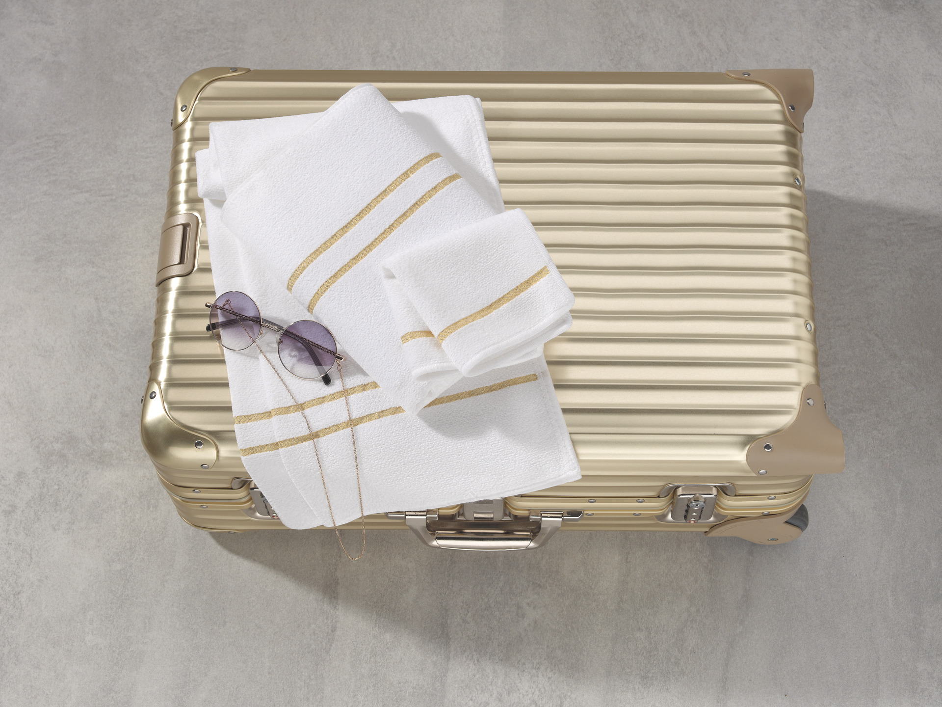White fabric with subtle gold stripes, elegantly placed on a metallic suitcase on a stone floor.