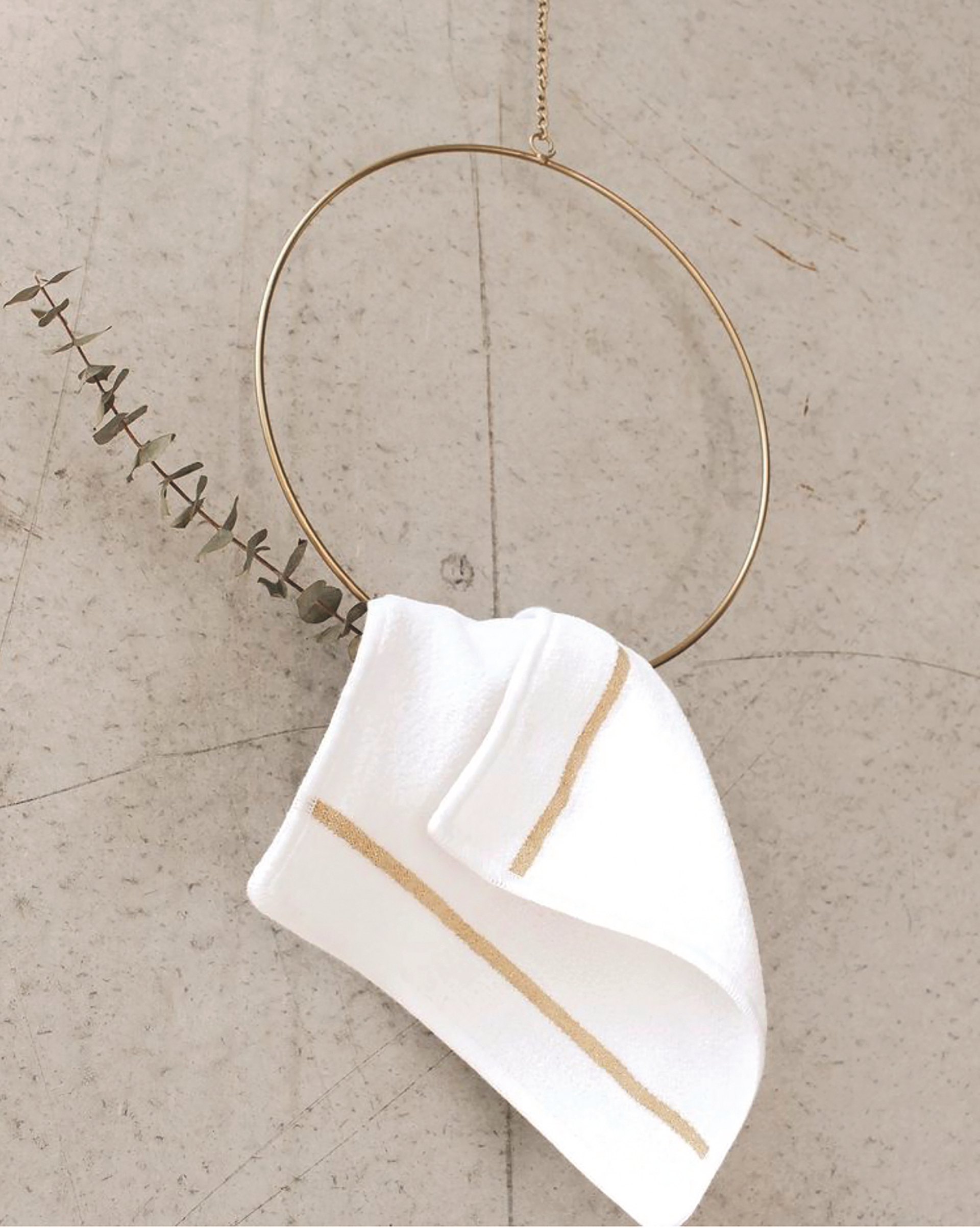 White chenille textile with gold stripes, draped on a golden ring with eucalyptus accent; minimalist display.
