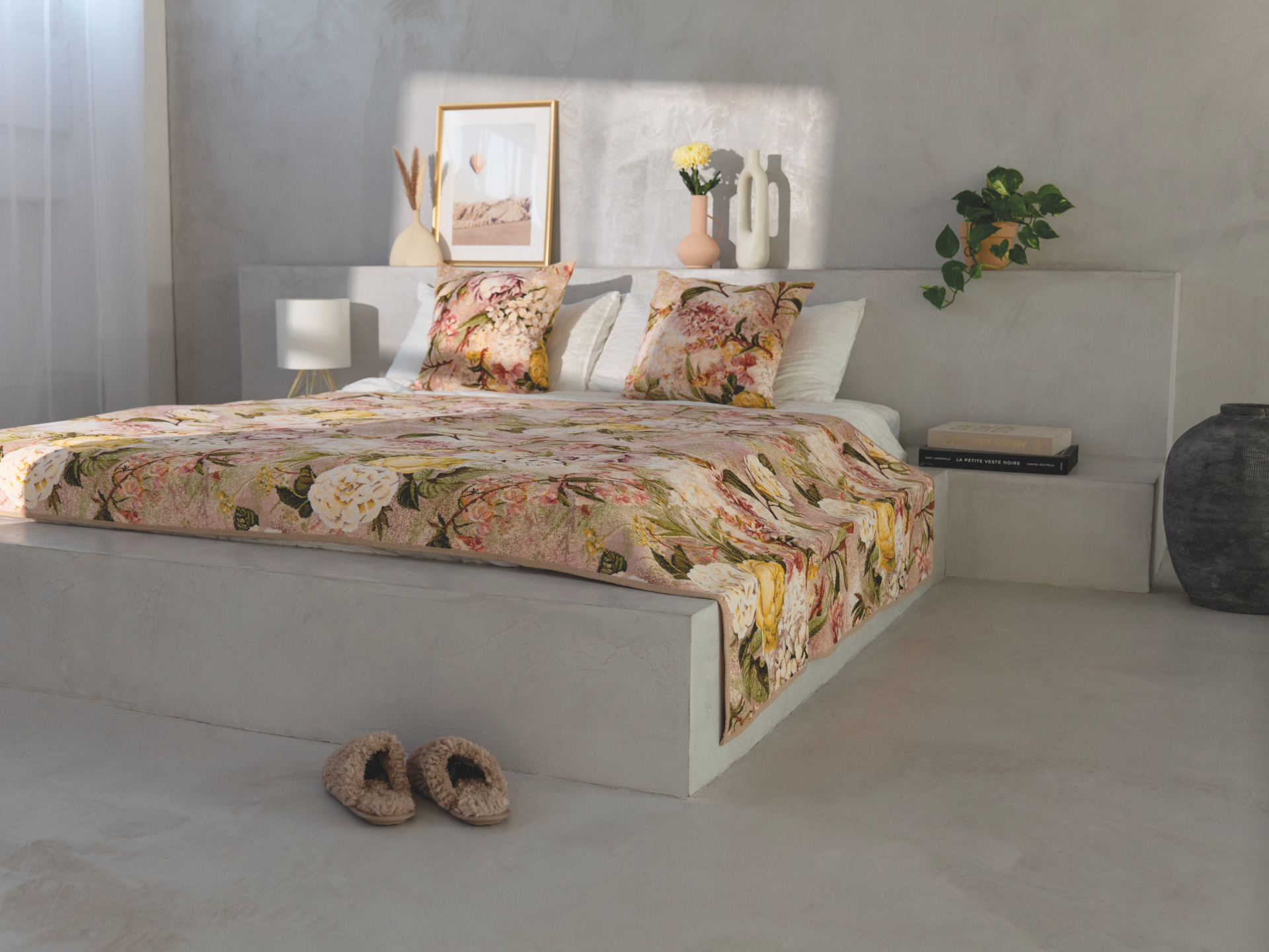 A bed with floral-patterned bedding in a minimalist room, featuring decorative pillows and soft light.