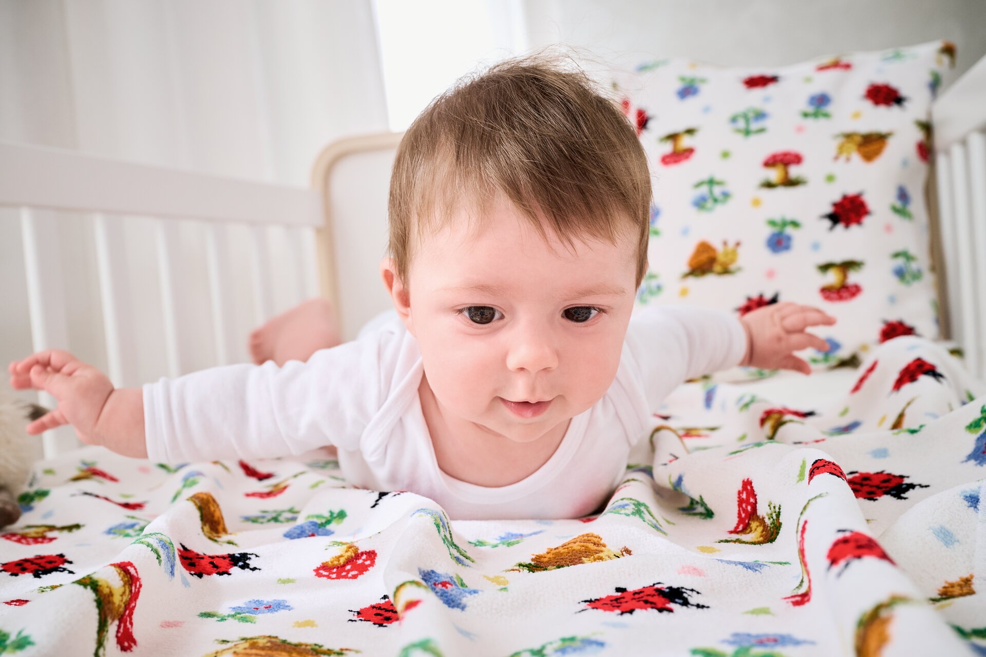 Baby auf bunter Bettwäsche im Kinderzimmer – Luxuriöses FEILER Handtuch der Kollektion PAULI DOTS als Lifestyleaufnahme aus Original FEILER-Chenille, Made in Germany.