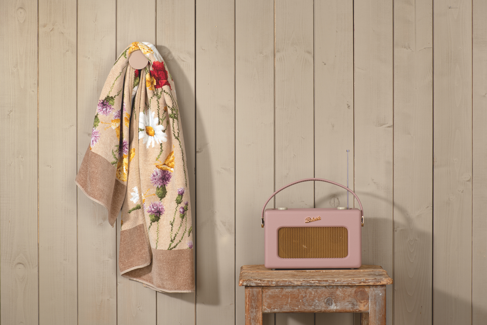Handtuch mit Blumenmotiv an Holzwand – Luxuriöses FEILER Handtuch der Kollektion DAISY FIELD in Beige als Lifestyleaufnahme aus Original FEILER-Chenille, Made in Germany.