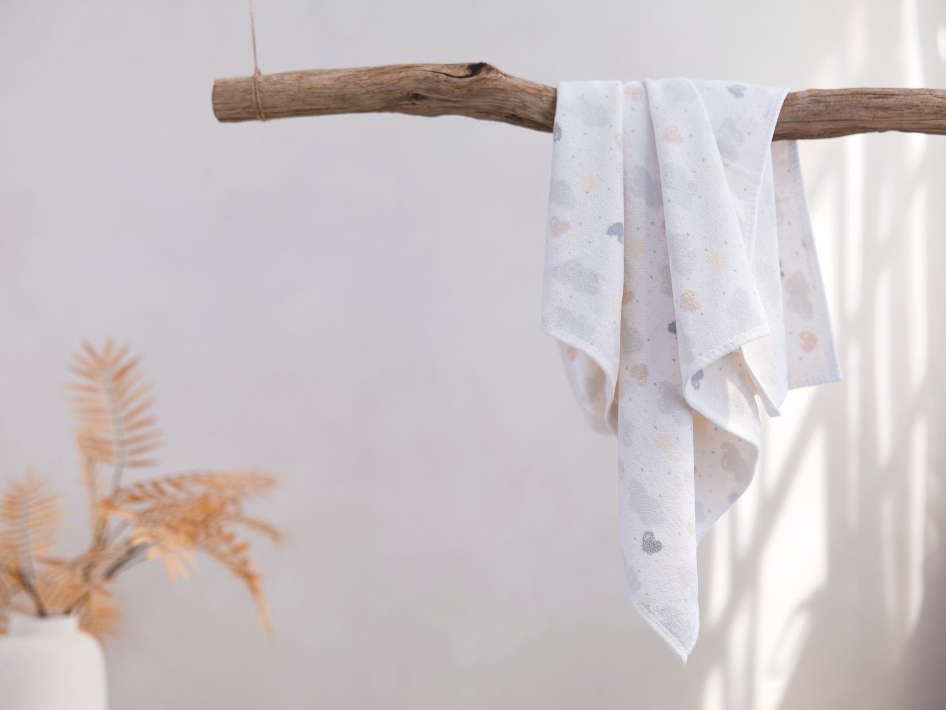 Hanging textile with subtle cloud and heart pattern in soft pastel shades. Earthy branch and dried plant nearby.