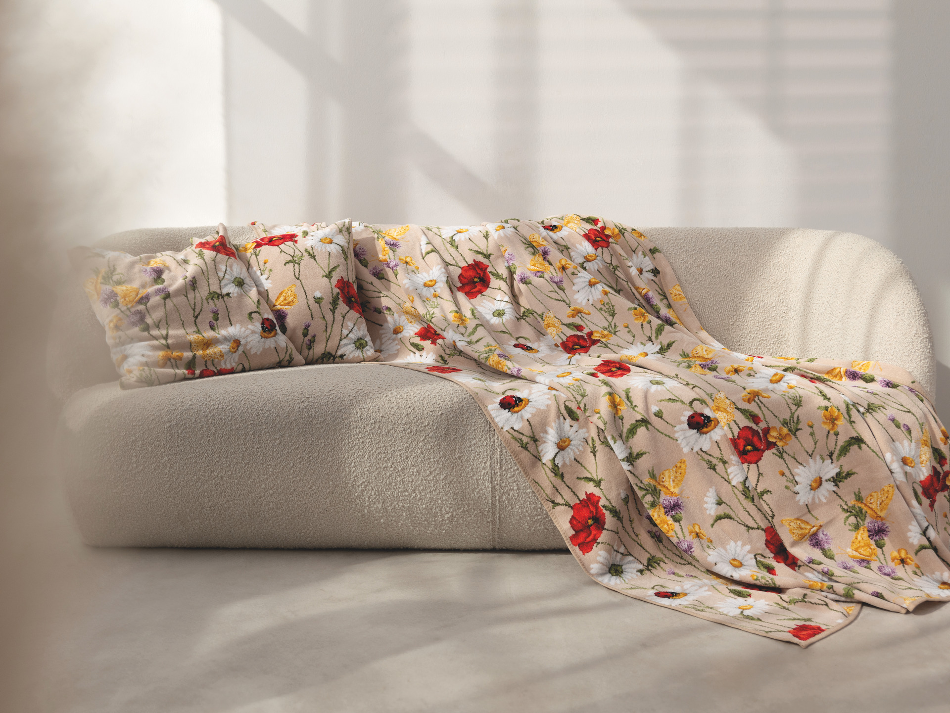 Blumige Chenille-Decke auf Sofa – Luxuriöse FEILER Decke der Kollektion DAISY FIELD in Beige aus Original FEILER-Chenille, Made in Germany.