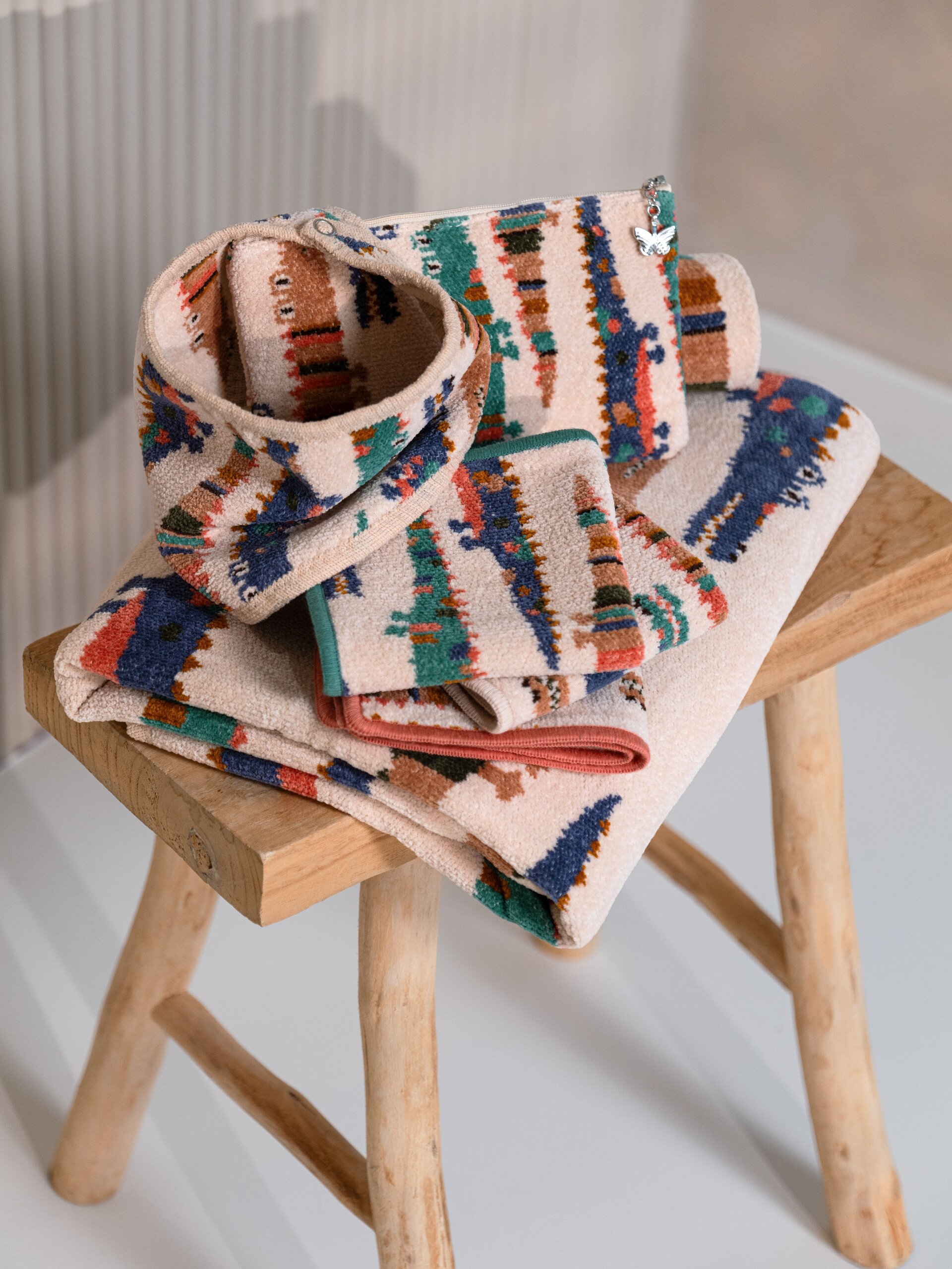 Lifestyle-Aufnahme verschiedener FEILER KROKO Babytextilien und Accessoires aus Original FEILER-Chenille, auf einem Hocker arrangiert.