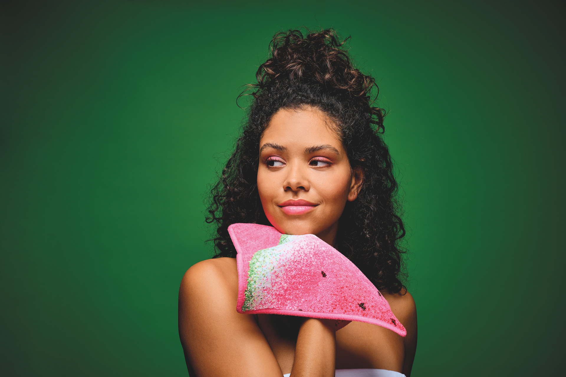Frau mit pinkem Accessoire vor grünem Hintergrund – Luxuriöses FEILER Handtuch der Kollektion FRUITS als Lifestyleaufnahme aus Original FEILER-Chenille, Made in Germany.