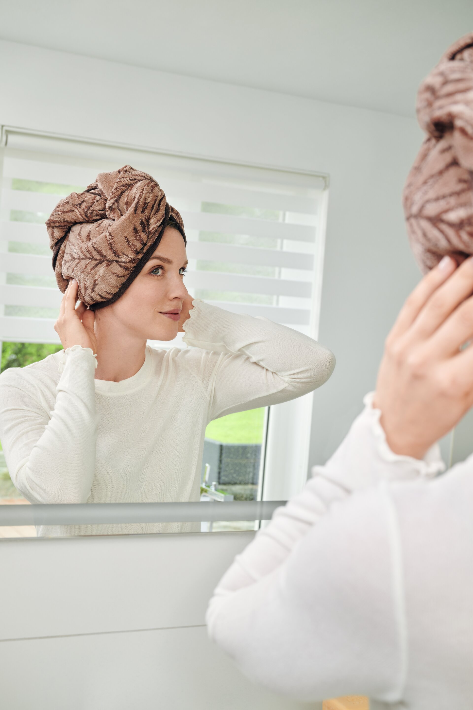 Erste Lifestyle-Aufnahme des FEILER OASIS NIGHTS Handtuch-Turbans aus Original FEILER-Chenille, getragen von einem Model im Badezimmer.